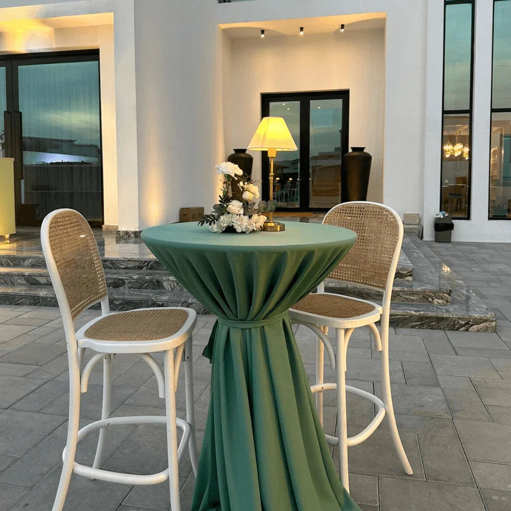 Sage Twilight- Cocktail Setup: Table with green cloth, eight stools, white flower centerpiece, and wireless lamp, arranged for a party setting.