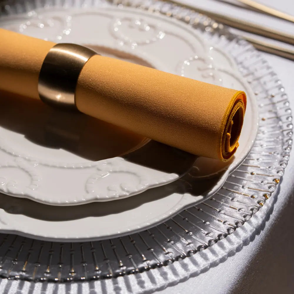 Clear radial gold charger plate elegantly set with white plates and mustard-yellow napkin, showcasing luxury tableware from Party Social for sophisticated events.