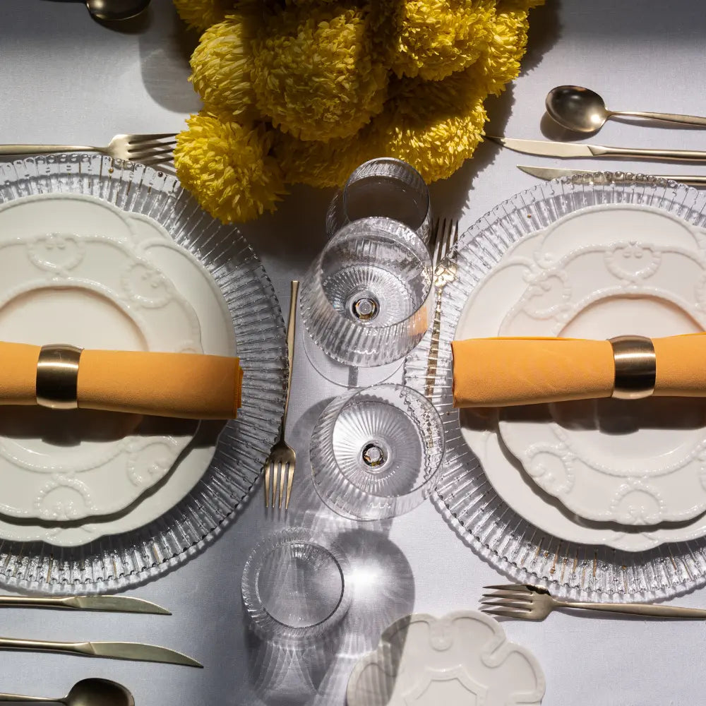 CHARGER PLATE- CLEAR RADIAL GOLD elegantly set on a table with embossed dinnerware, gold flatware, yellow napkins, and a vibrant yellow floral centerpiece.