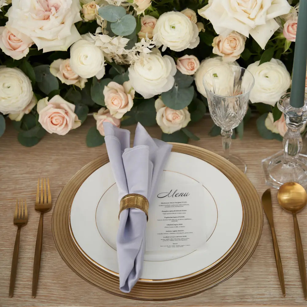 CHARGER PLATE - GOLD LINED: Elegant gold-trimmed plate enhances formal place setting with a menu card, gold flatware, and floral centerpiece, perfect for weddings or special events.