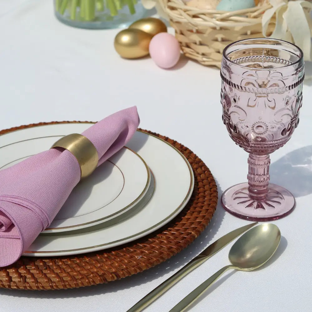 CUTLERY MODERN CHAMPAGNE: Matte gold spoon and knife set elegantly complementing a woven rattan charger and vintage-style glass, perfect for stylish dining occasions.