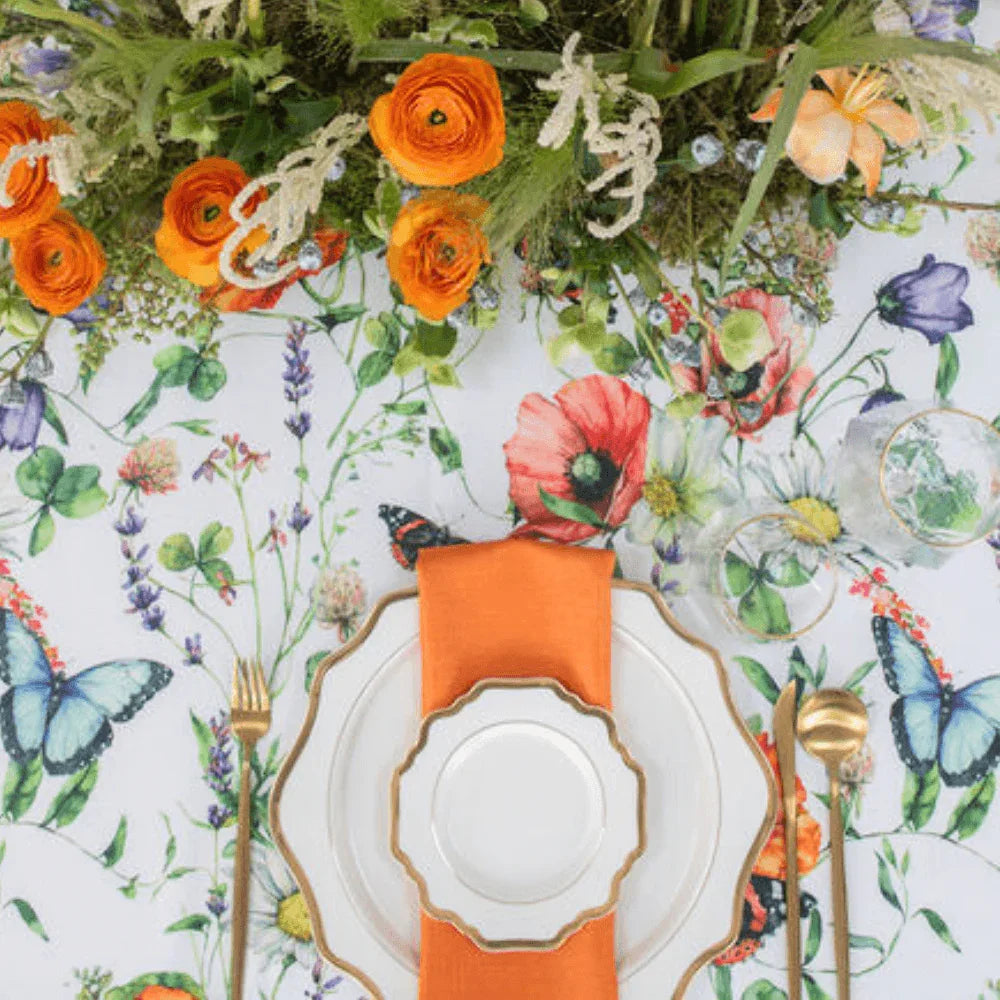 Butterfly Meadows- Dining Setup featuring a table set for eight with floral centerpiece, gold-trimmed plates, gold cutlery, and napkins, perfect for elegant gatherings.