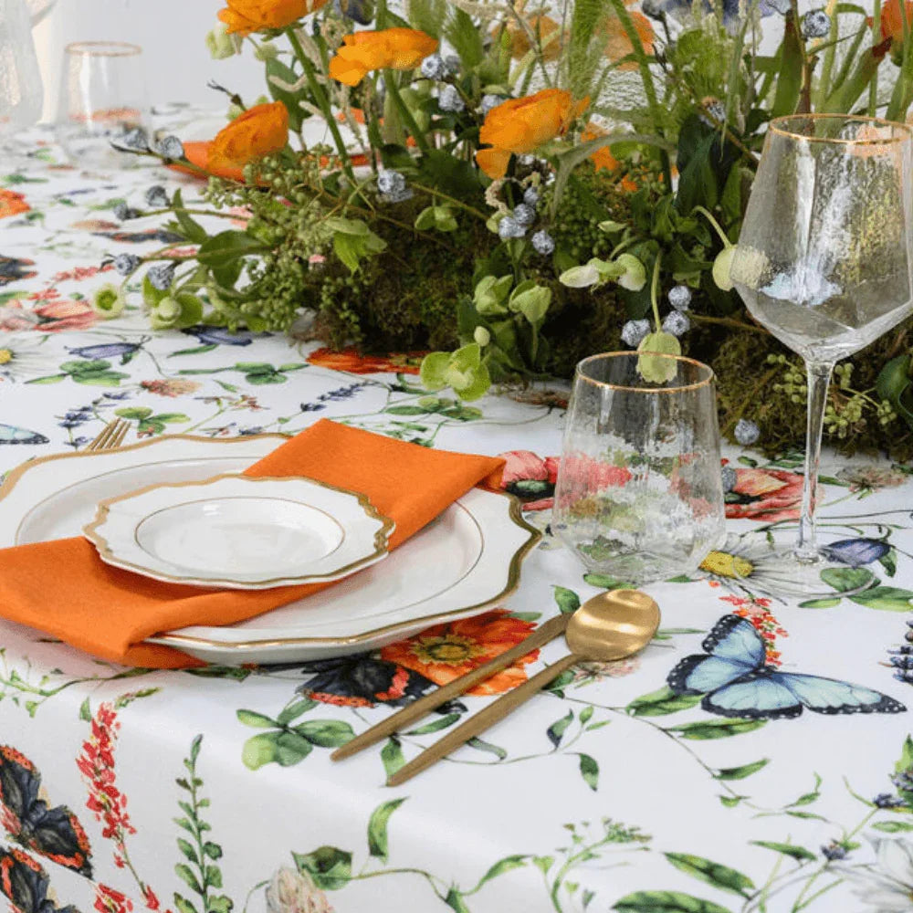 Butterfly Meadows- Dining Setup: Elegant table setting for eight with plates, gold cutlery, wine glasses, napkins, acrylic chairs, and a floral centrepiece.