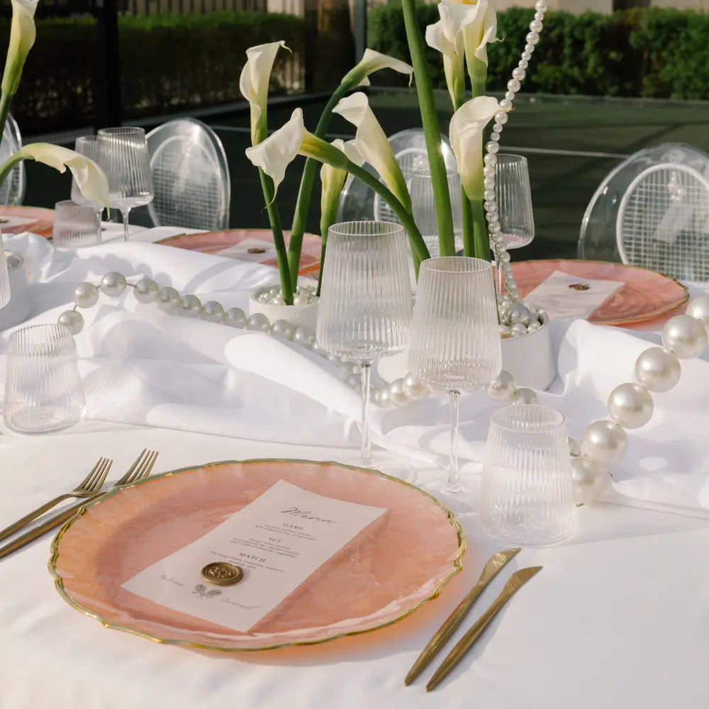 CHARGER PLATE - PINK PEARL W/ GOLD RIM elegantly set with gold flatware and ribbed goblets, creating a sophisticated table setting for upscale events.