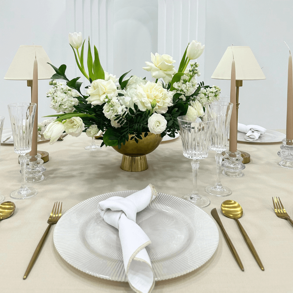 Sand Elegance- Dining Setup featuring a flower centerpiece, gold cutlery, wine glasses, and napkins arranged on a table for eight guests.