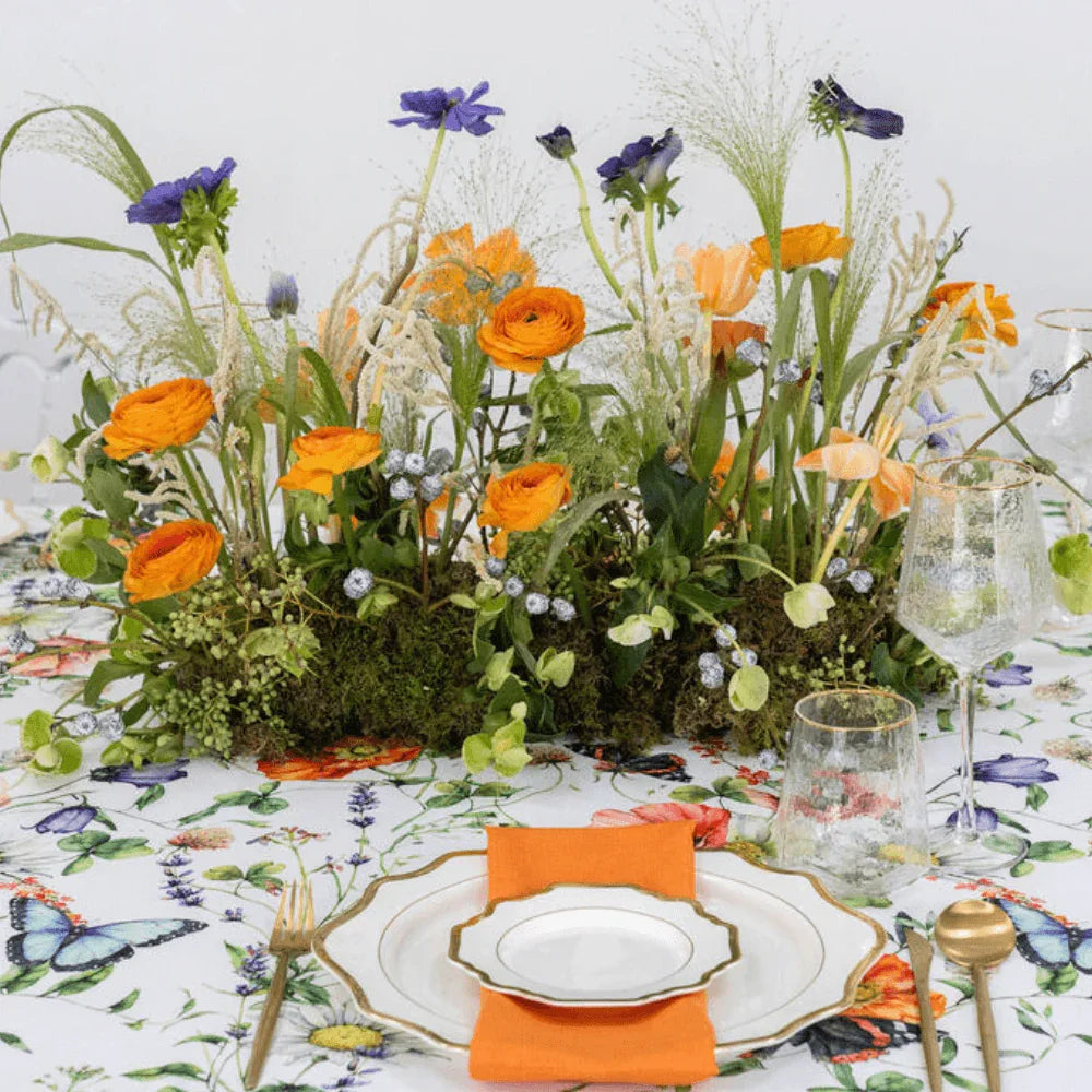 Butterfly Meadows-Dining Setup with a flower centerpiece on a table, surrounded by plates, gold cutlery, glasses, and napkins for eight guests.