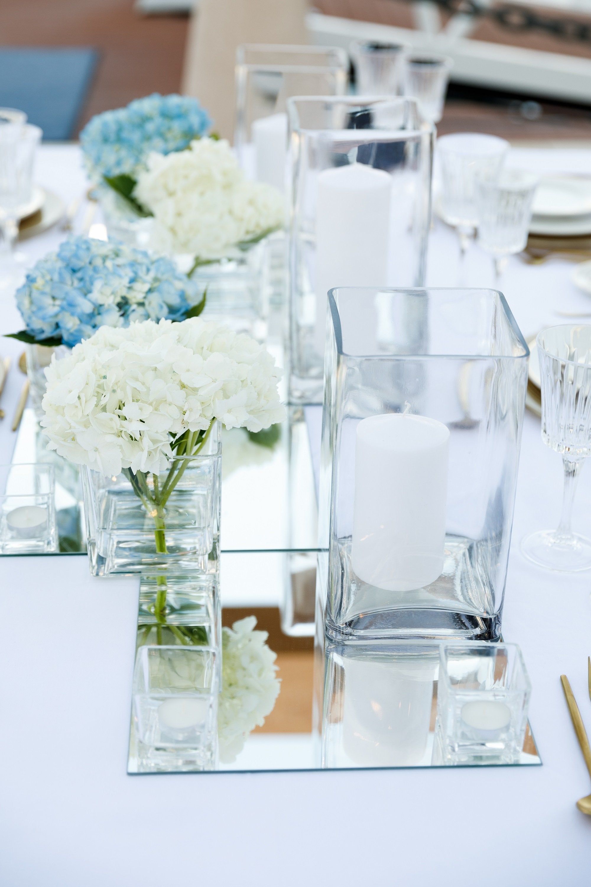 Square glass vase on a table with white and blue flowers, showcasing an elegant event accessory for home or event décor. Candles not included.
