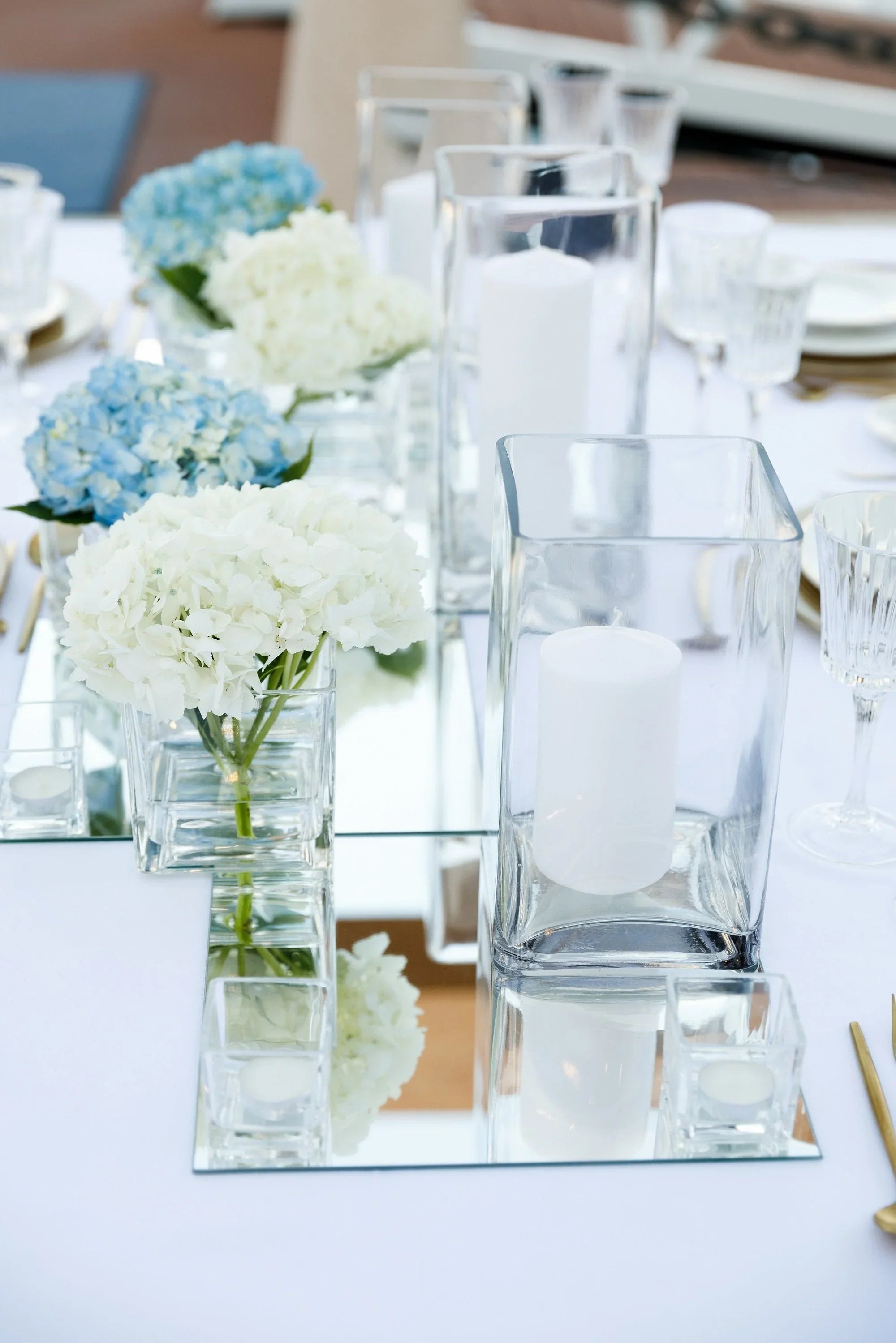 Square glass vase on a table with white and blue flowers, showcasing an elegant event accessory for home or event décor. Candles not included.