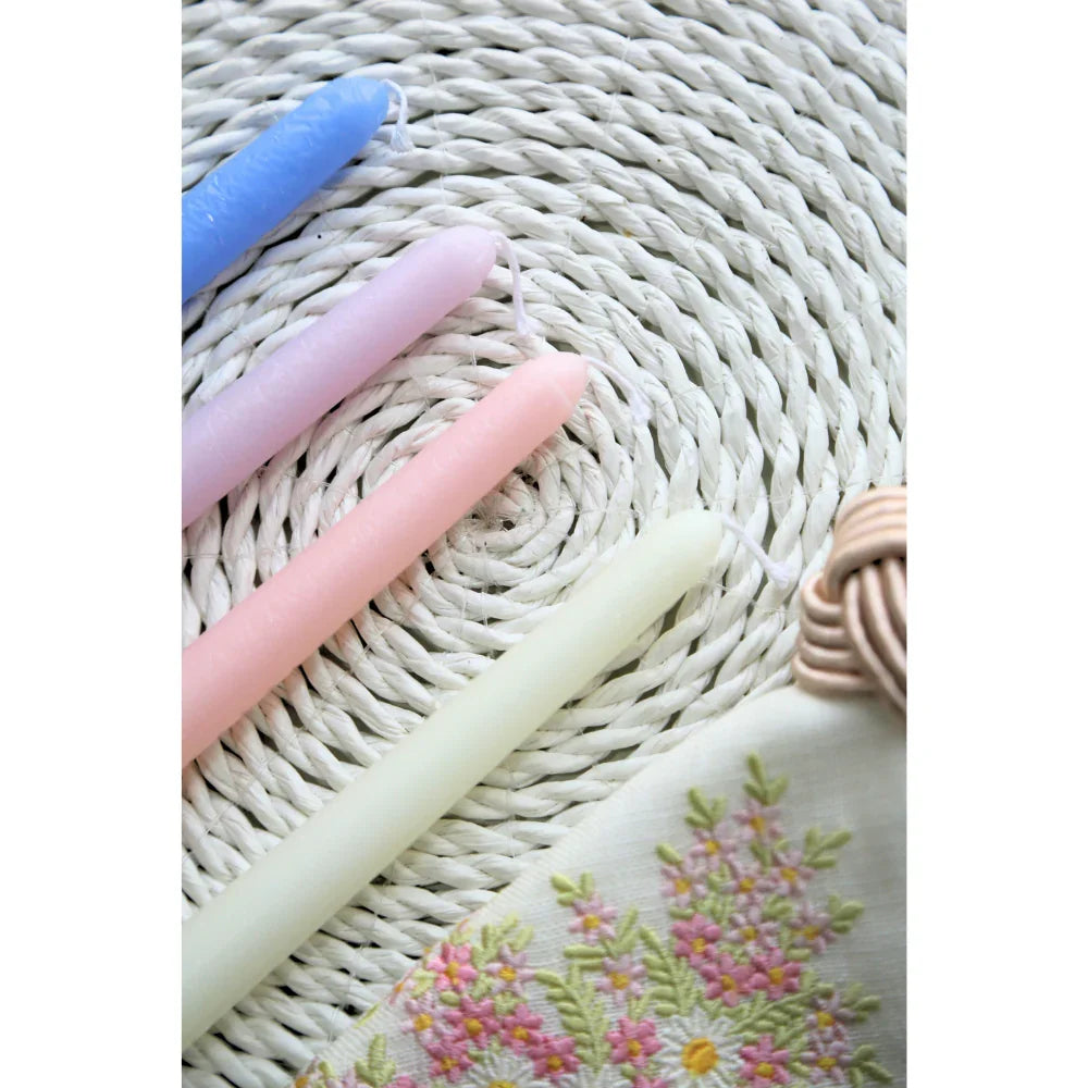 The Tapered Flame Smokeless Candles, artisanally crafted for elegant settings, rest atop a woven mat with a floral-embroidered napkin nearby, ideal for events.