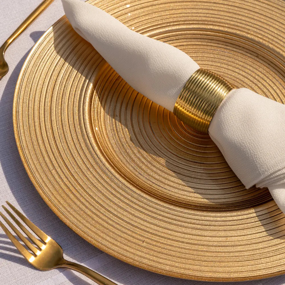 CHARGER PLATE - GOLD LINED: Elegant metallic gold charger with textured concentric rings, featuring a white napkin with gold ring and gold-plated flatware, enhancing any dining occasion.