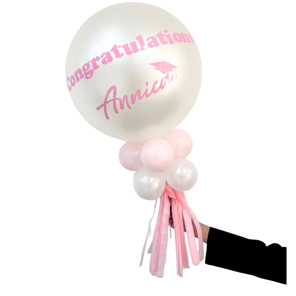 Personalized Balloon Wand featuring a large pearl-white balloon with congratulations Annica, surrounded by smaller balloons and streamers, held by a hand.