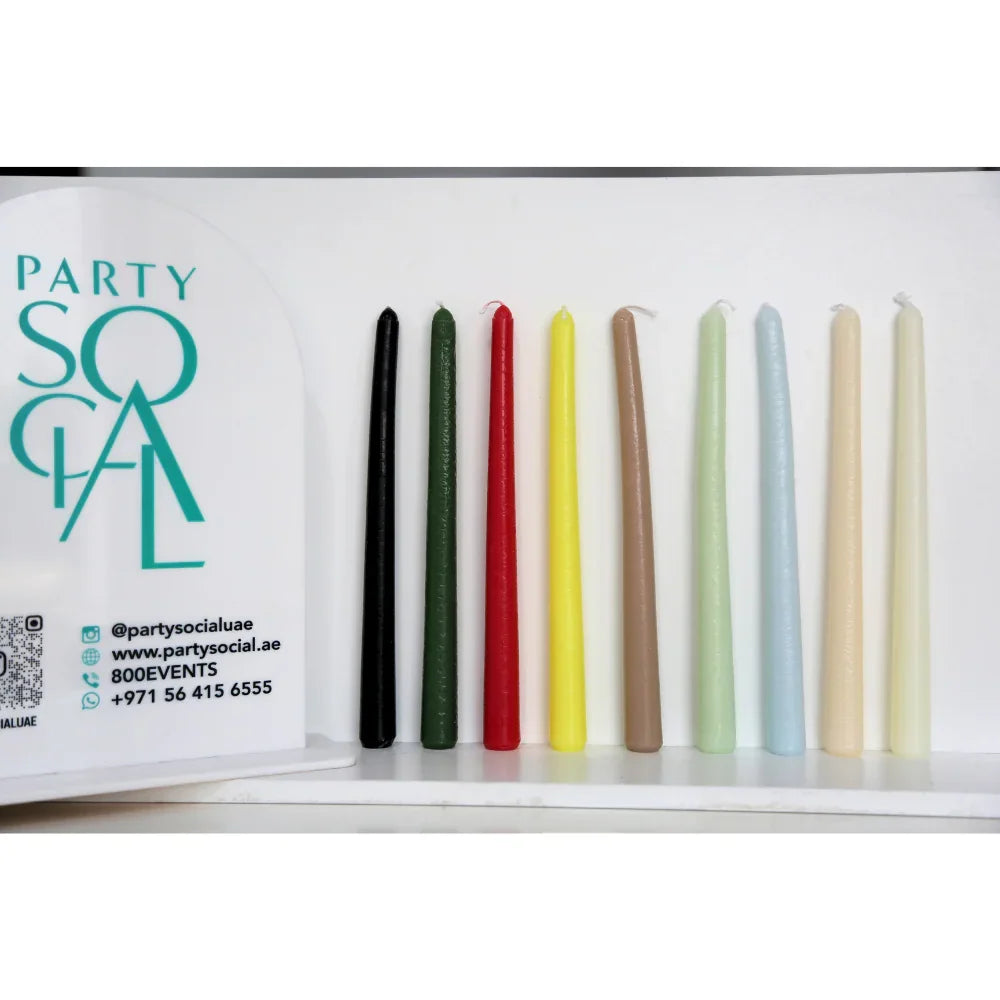 The Tapered Flame Smokeless Candles in various colors on a white shelf, showcasing elegant, artisan Belgian craftsmanship for a warm ambiance.