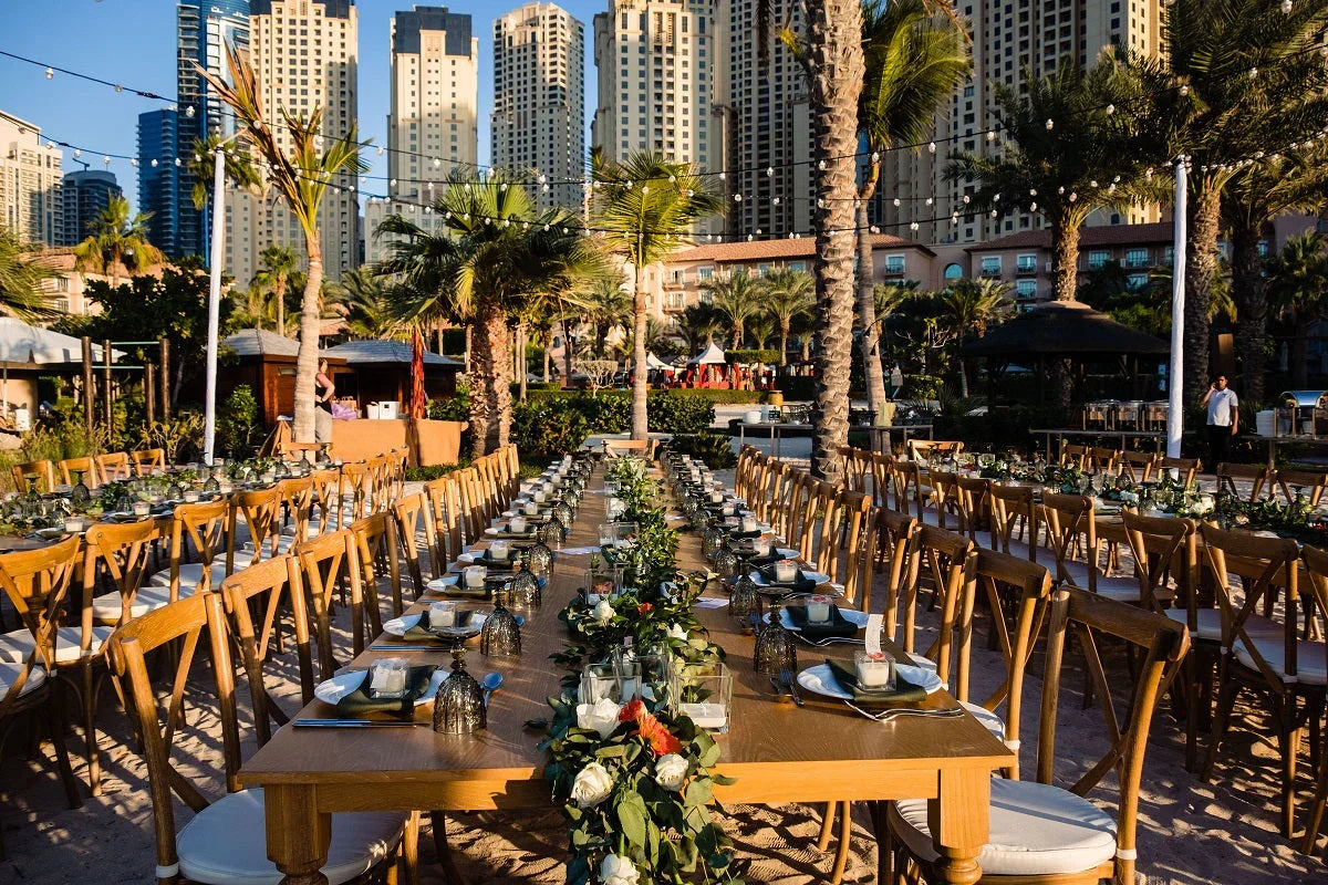 WOODEN DINING TABLE set up for an outdoor event, seating up to eight, featuring floral centerpieces and candles, perfect for parties and gatherings.