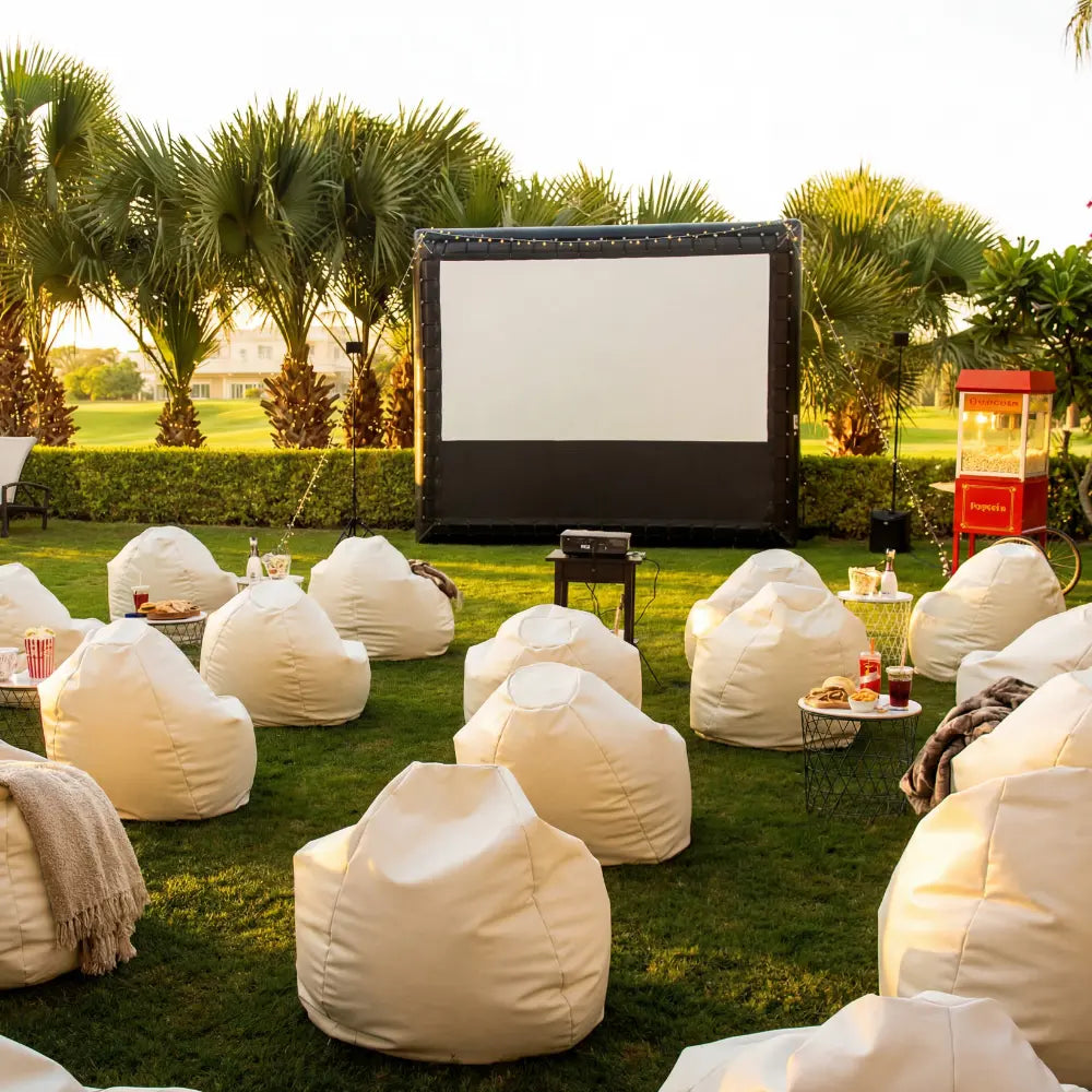 BEANBAG WHITE chairs arranged for an outdoor movie night, complemented by wire-frame tables with snacks, creating a cozy party atmosphere on a lawn.