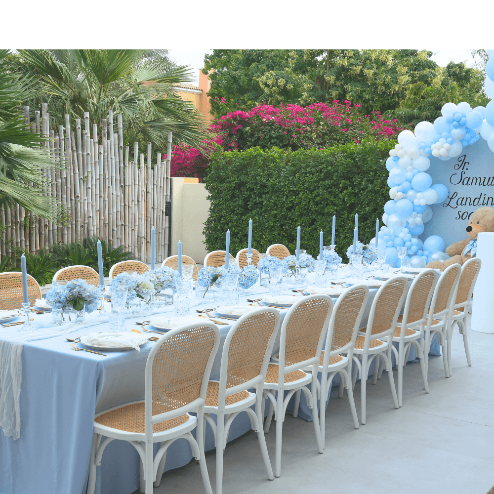 Outdoor dining setup with tables, chairs, and decorative balloons in a garden setting.