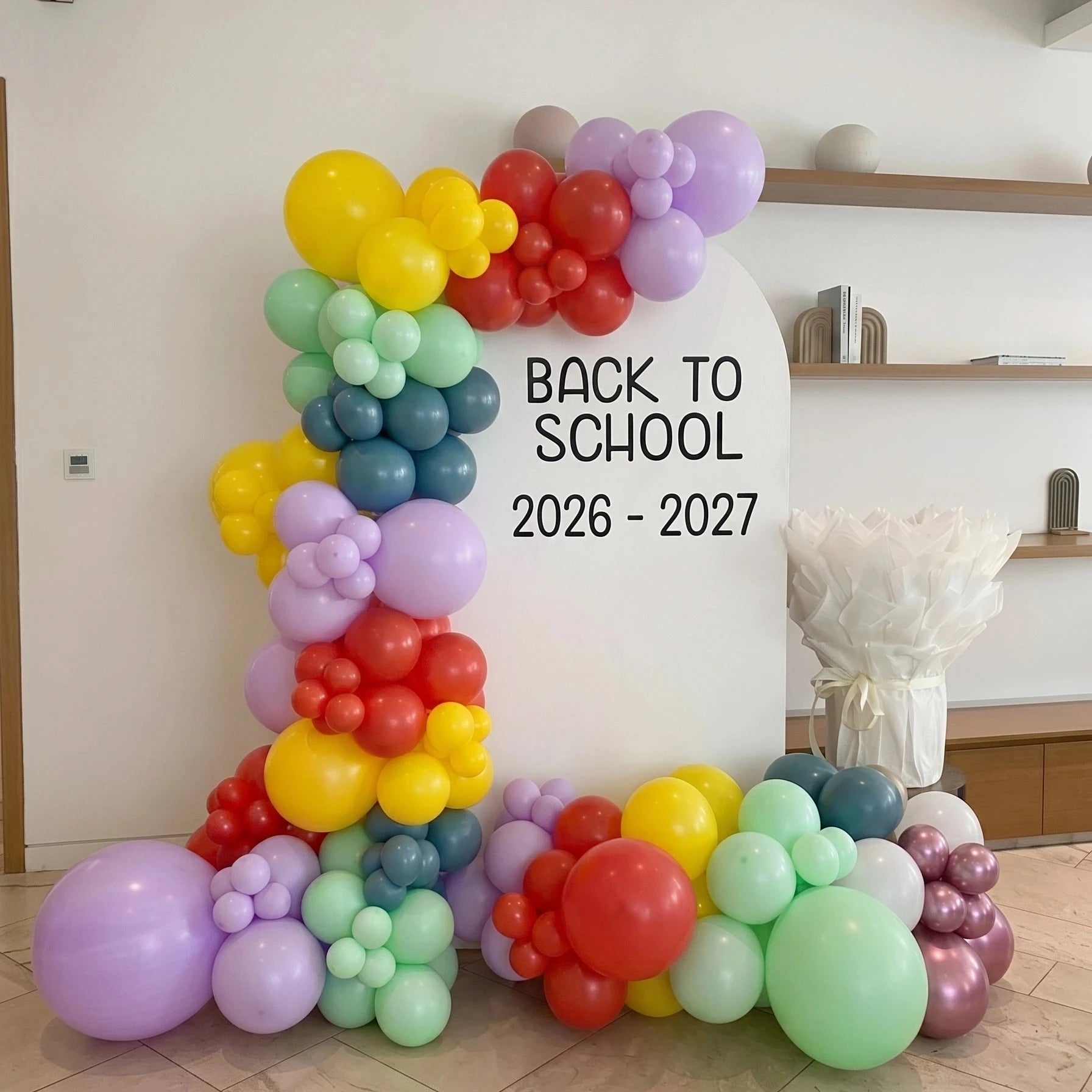 A colorful balloon arch backdrop with the text &