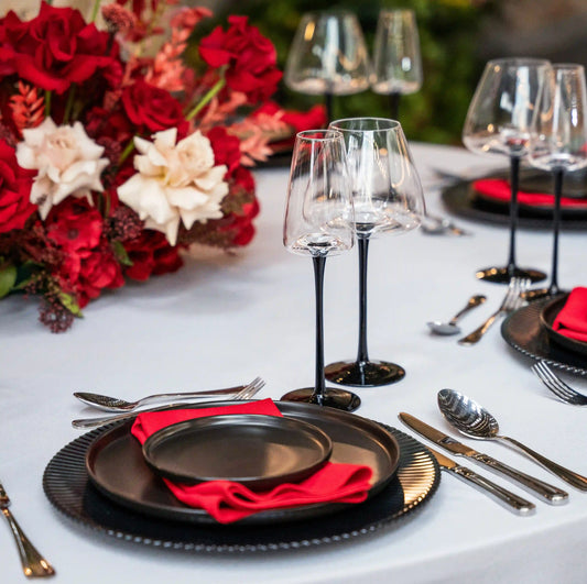 Black Stem Glassware Collection with matte black stems and clear bowls on an elegantly set table with black plates and red napkins for stylish events.