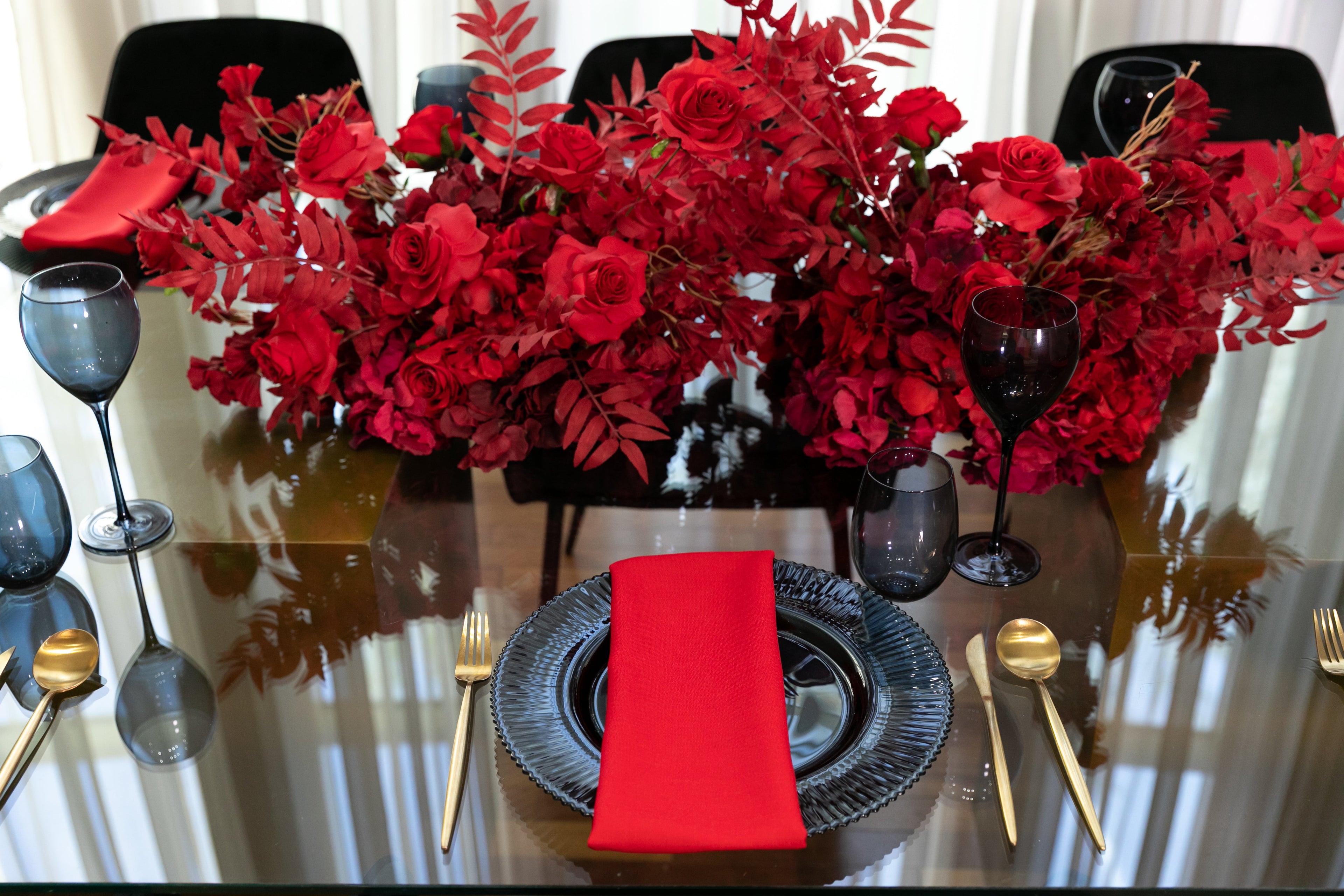Black & Gold Collection table setup featuring red roses, wine glasses, and a red napkin on a black plate, ideal for an elegant party atmosphere.
