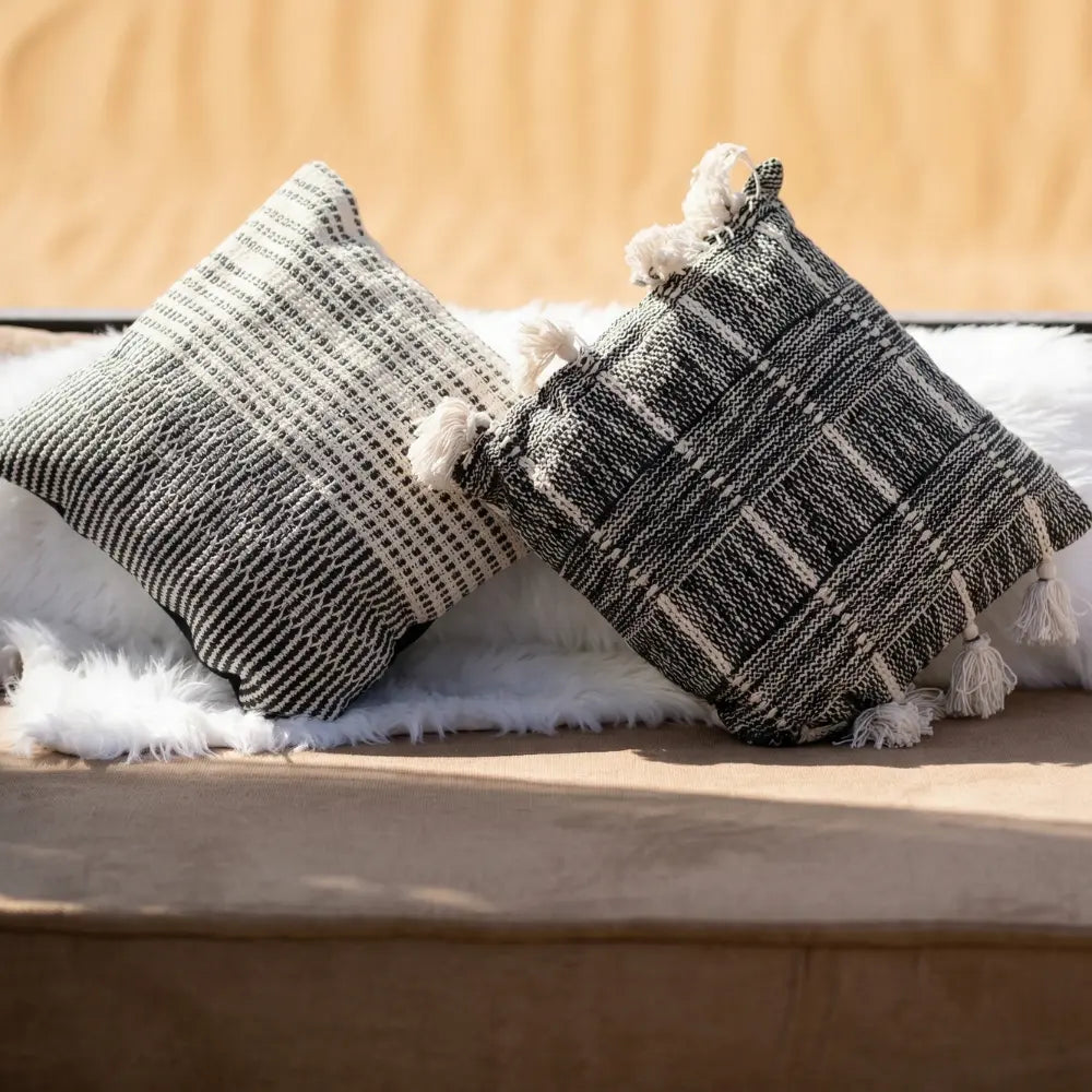 CUSHION BOHO COVER: Black-and-white woven cushions with tassels on a fluffy throw, ideal for enhancing sofas or lounge seating. Available with a ready-to-use filler.