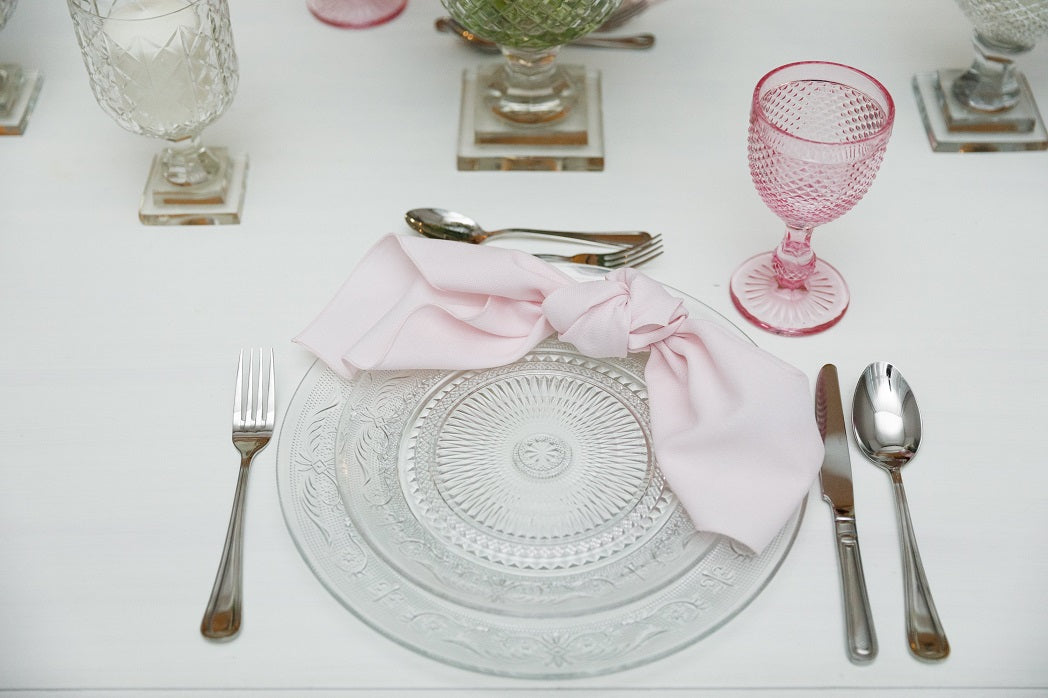 Vintage clear glass plates with pink napkin; features fork and spoon setup. Ideal for elegant table settings.