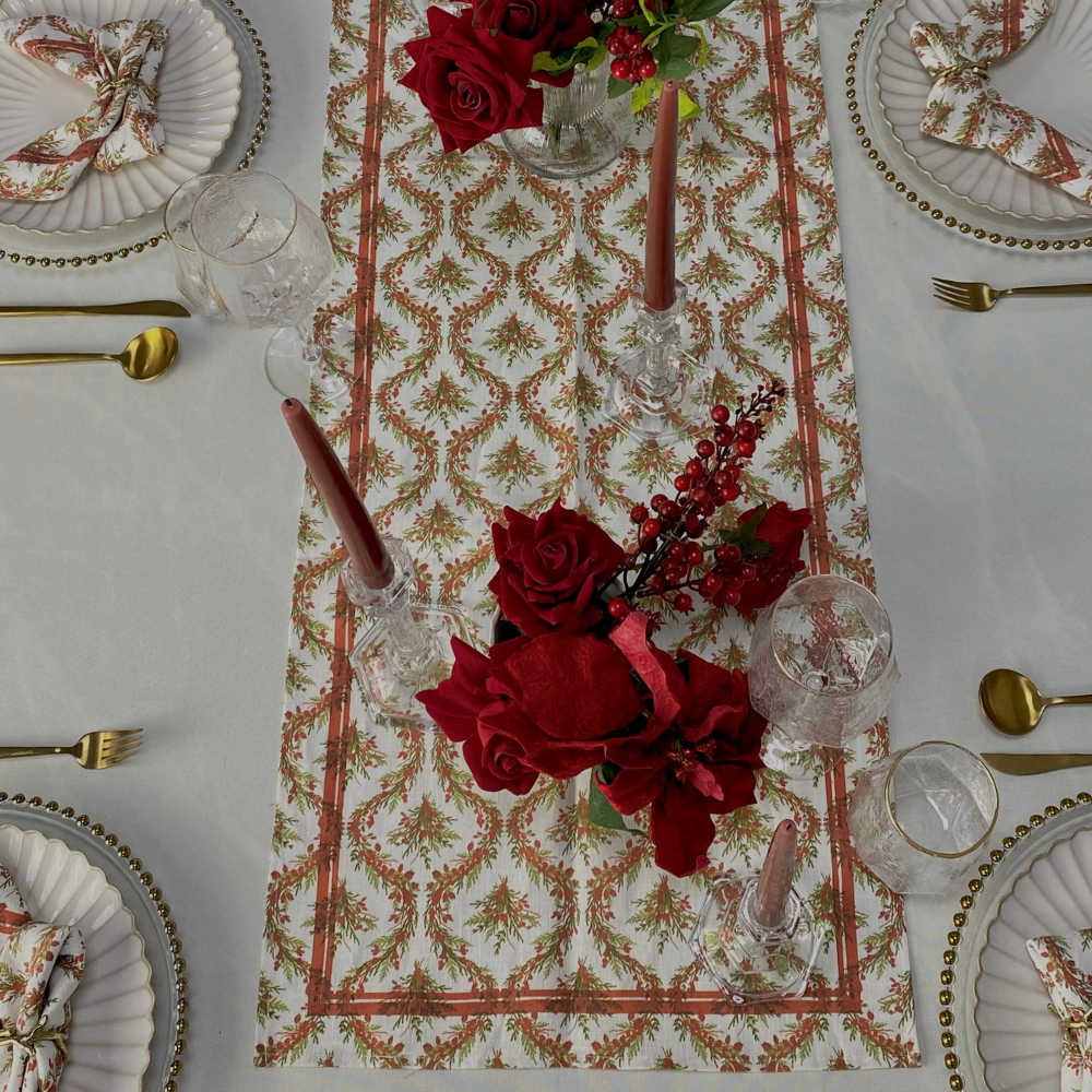 Festive table setting featuring the Holly & Pine Linen Runner, enhancing elegance with patterned napkins, gold flatware, and a rose centerpiece for a luxurious holiday meal.
