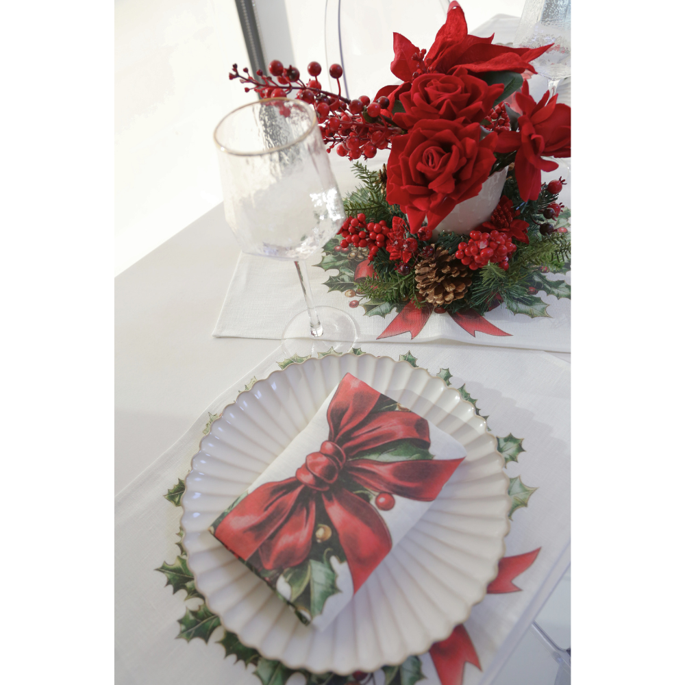 Evergreen Knot Linen Placemat enhances a holiday table with holly and red ribbon motifs, complementing festive dinnerware and a Christmas-themed centerpiece.