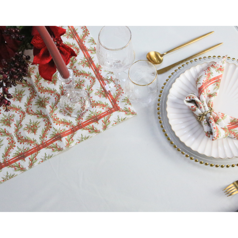 Holly & Pine Linen Napkin elegantly folded with a gold ring on a festive table setting, featuring a red-and-green motif, ideal for Christmas celebrations.