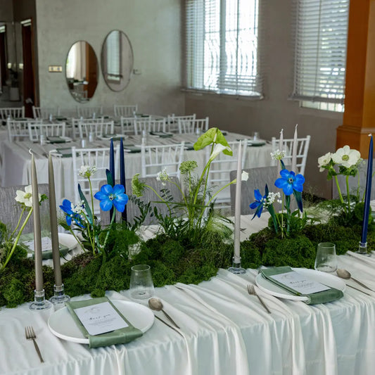 Classic Baby Shower Dinner Setup featuring a formal table with lush greenery, blue and white florals, taper candles, and elegant place settings with napkins and menu cards.