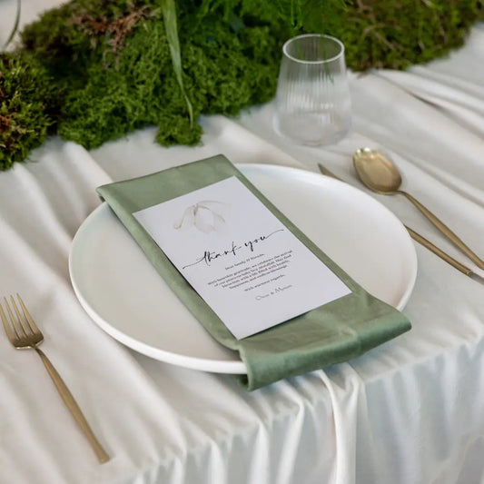 Classic Baby Shower Dinner Setup featuring a formal place setting with gold-tone cutlery, sage napkin on white plate, and greenery, creating a minimalist, elegant atmosphere.