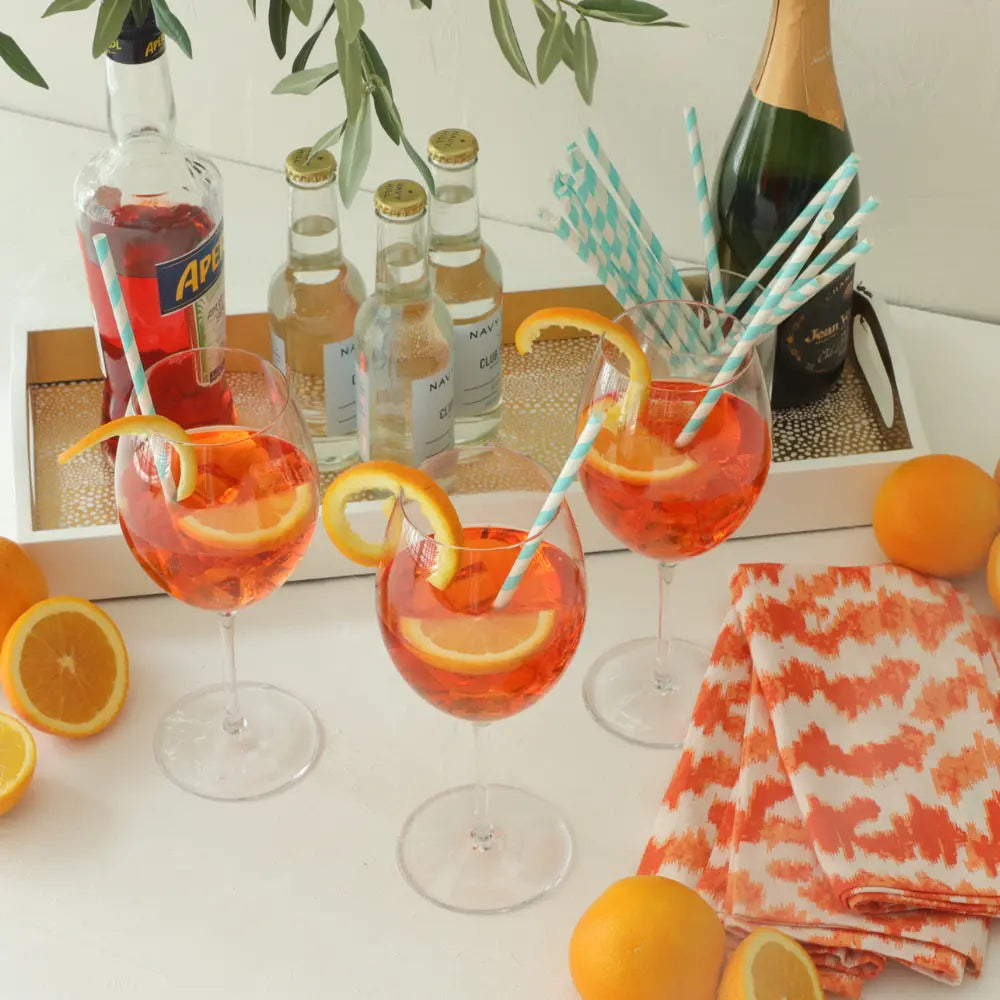 Cocktails with orange slices and blue straws on a table with bottles and oranges.