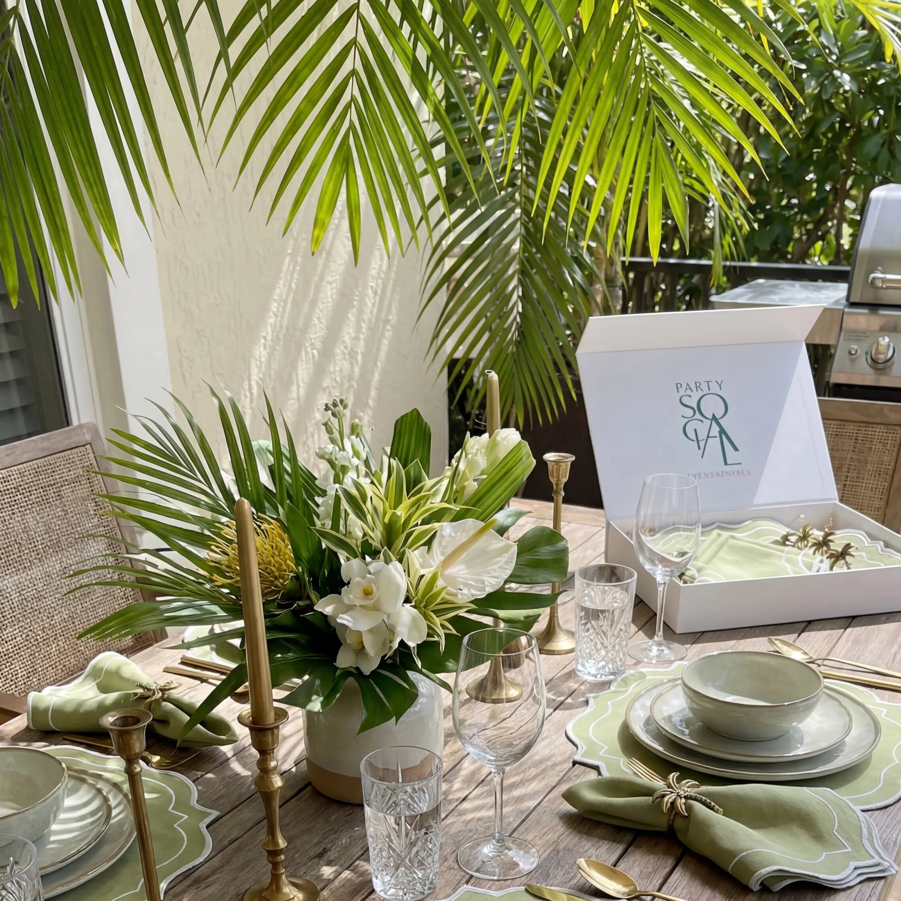 Tropical-themed table with Palm Serenity Gift Set featuring scalloped placemats, linen napkins, gold napkin rings, and elegant glassware, perfect for Ramadan gatherings.