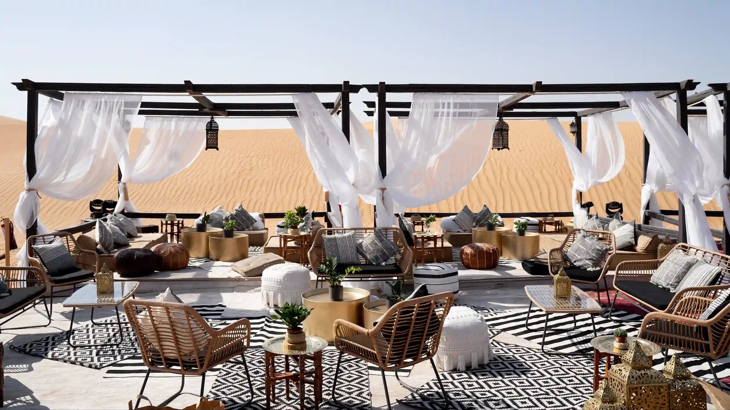 Outdoor patio area with wicker furniture, tables, and white curtains against a desert backdrop.