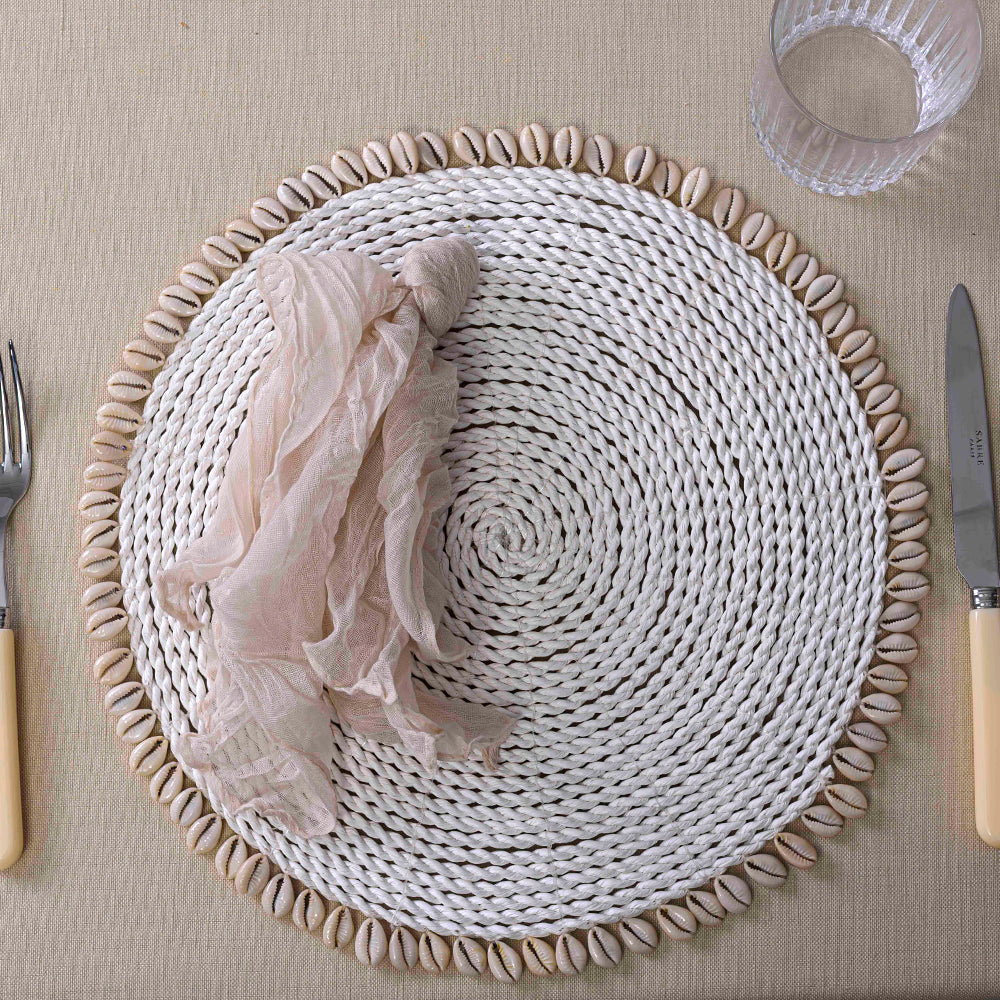 Woven seagrass placemat with seashells, glass, fork, and napkin on top.