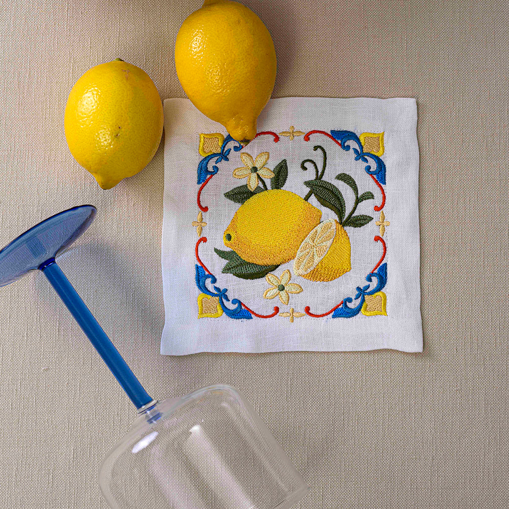 Majolica Lemon Pure Linen Coaster - 4 per pack, a pair of lemons on a napkin next to a glass, close-up views of lemons.