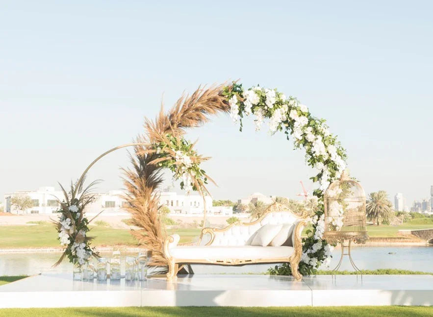 Round gold arch adorned with flowers, set behind a white couch with pillows, ideal for event decor.