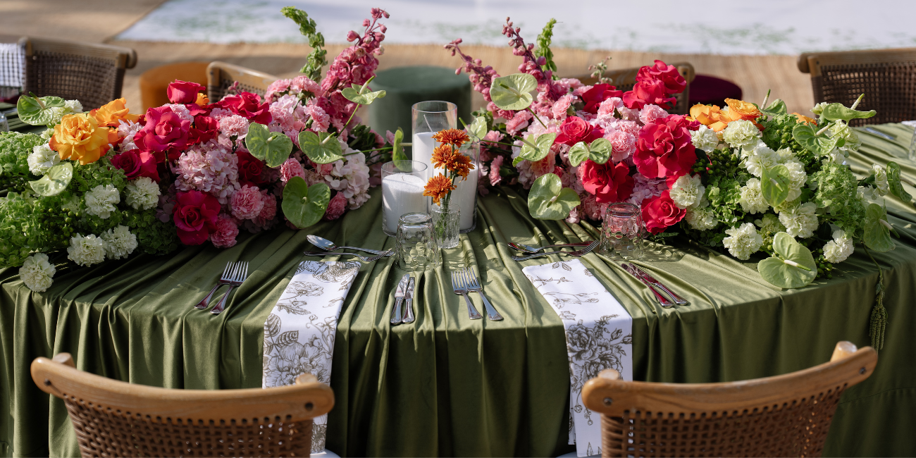Decorated table with floral arrangements and green tablecloth by a body of water.