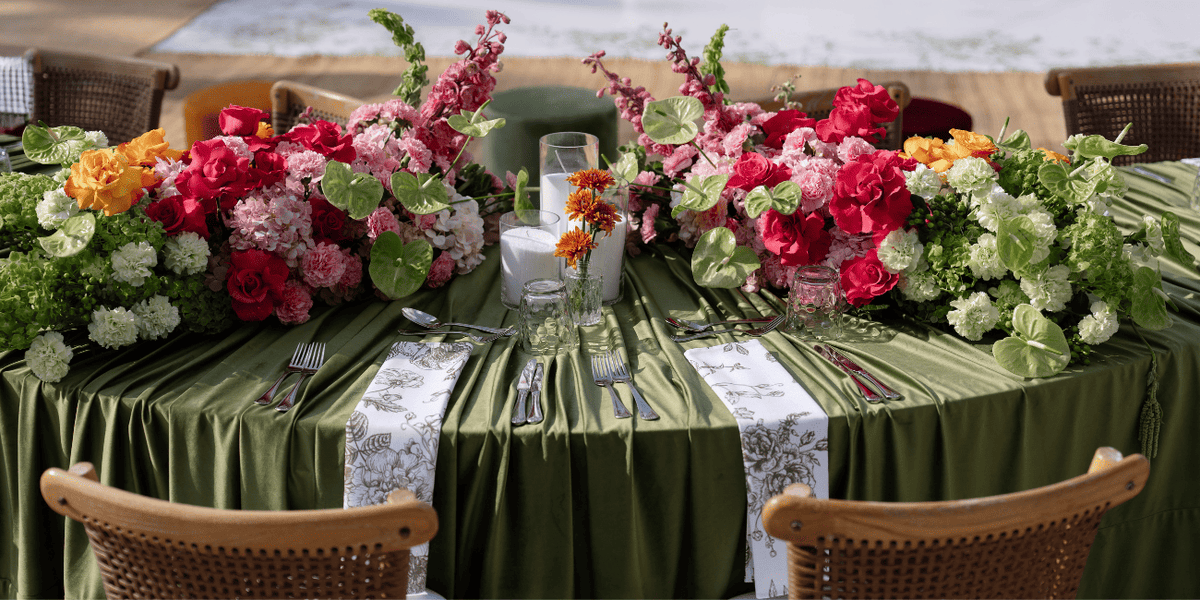 Decorated table with floral arrangements and green tablecloth by a body of water.