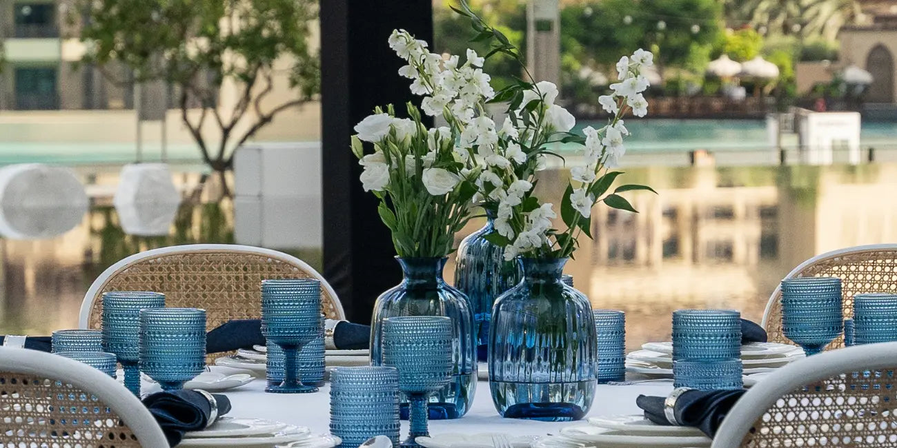 Dining table set with blue glassware and white flowers in a garden setting