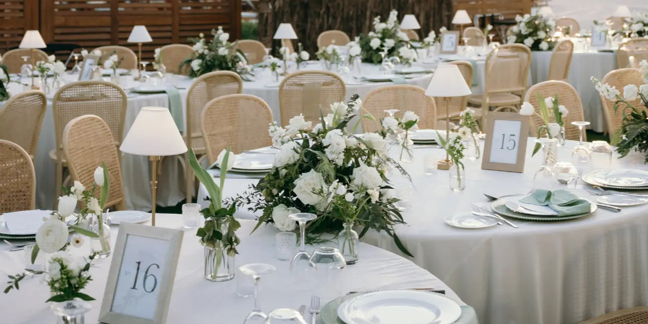 Decorated wedding reception tables with white tablecloths, floral centerpieces, and place cards.