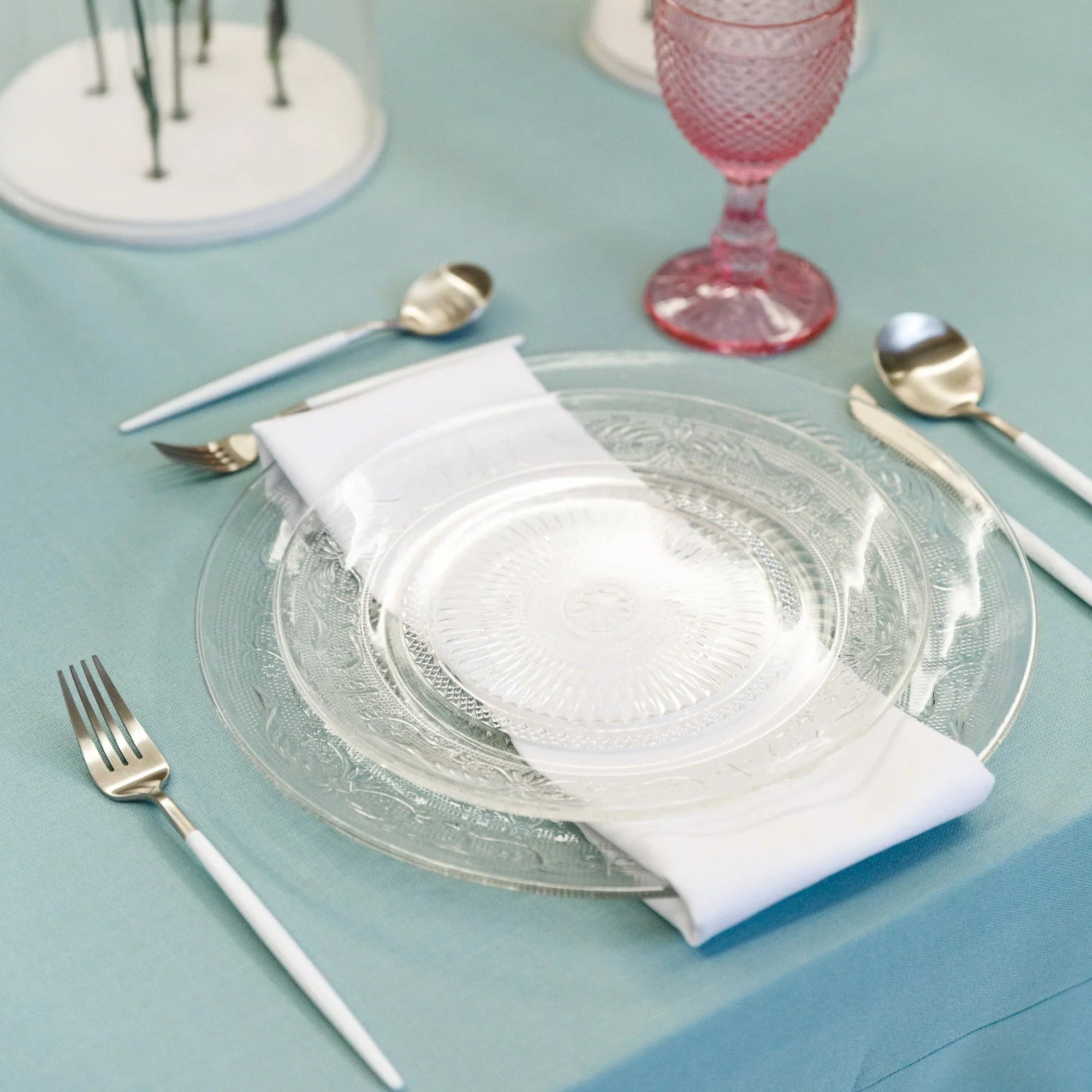 Vintage clear glass plates, delicately etched, displayed on a table with matching glassware and utensils, ideal for elegant table settings at events or special occasions.