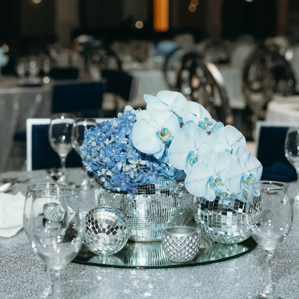 Disco ball decorative table centerpiece with blue flowers and mirror balls on a tablecloth.