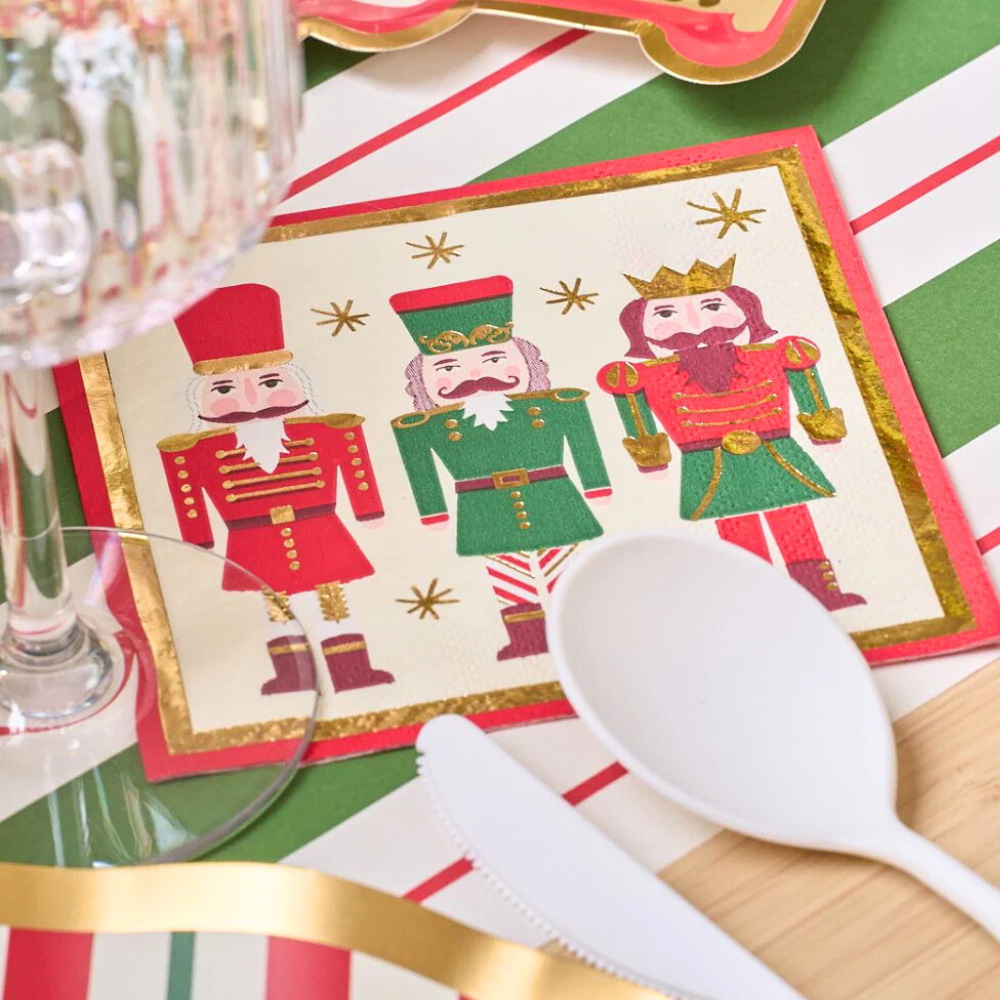Nutcracker Cocktail Napkins on a table with a glass, plate, and cutlery, highlighting their festive design perfect for holiday gatherings.