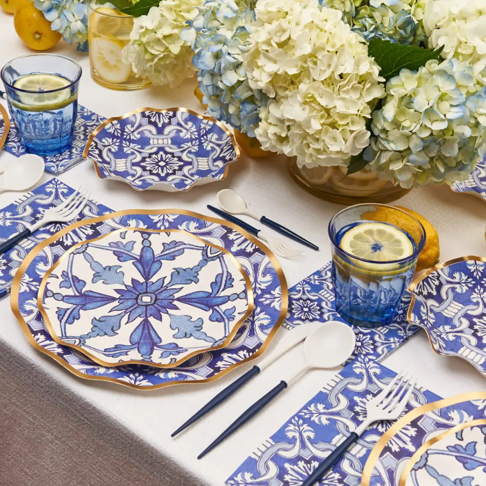 Decorative disposable table setting with blue and white patterned plates, glasses, and flowers.
