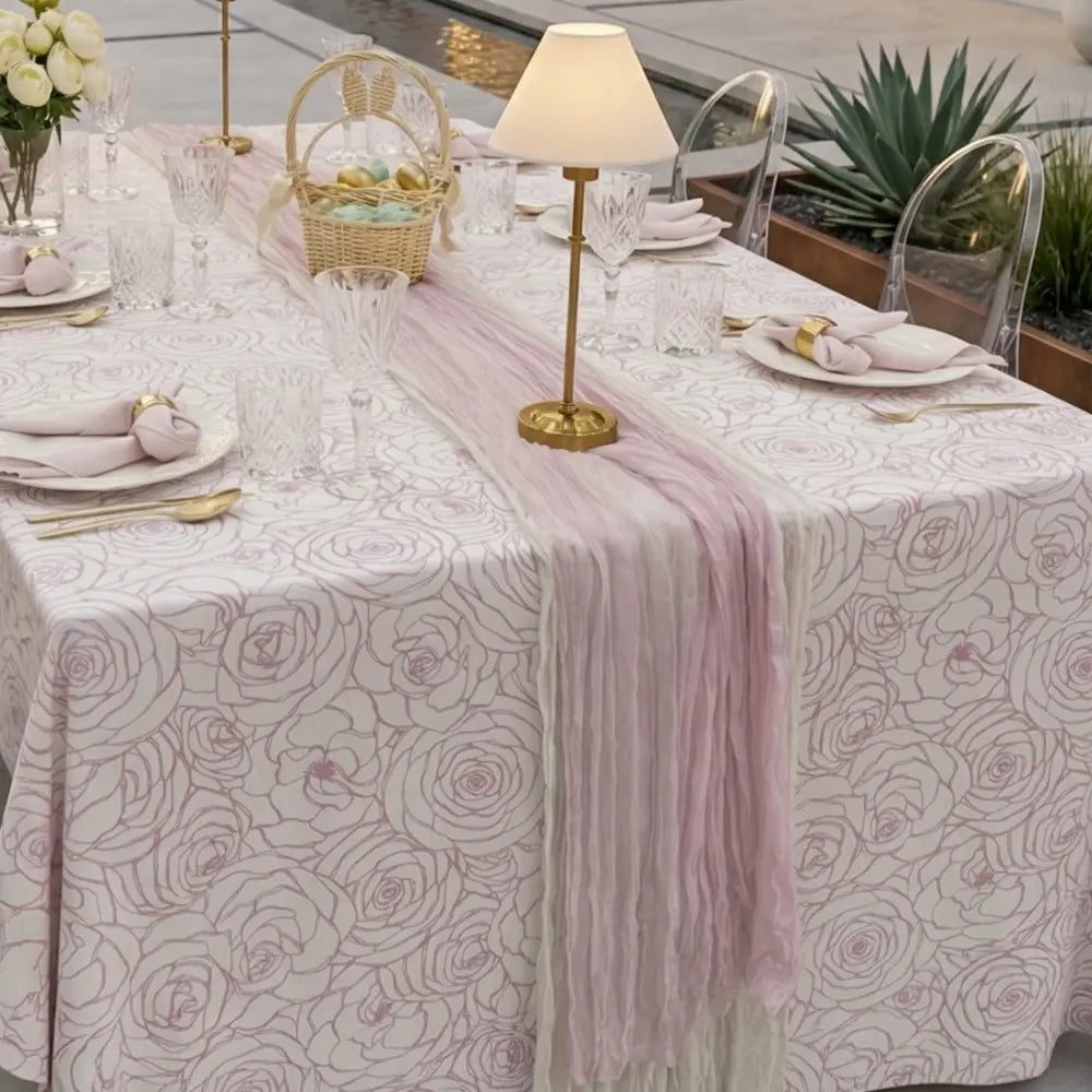 GAUZE TABLE RUNNERS elegantly drape a styled dining table with pink ombré hues, enhancing a sophisticated outdoor setting with gold flatware and crystal glassware.