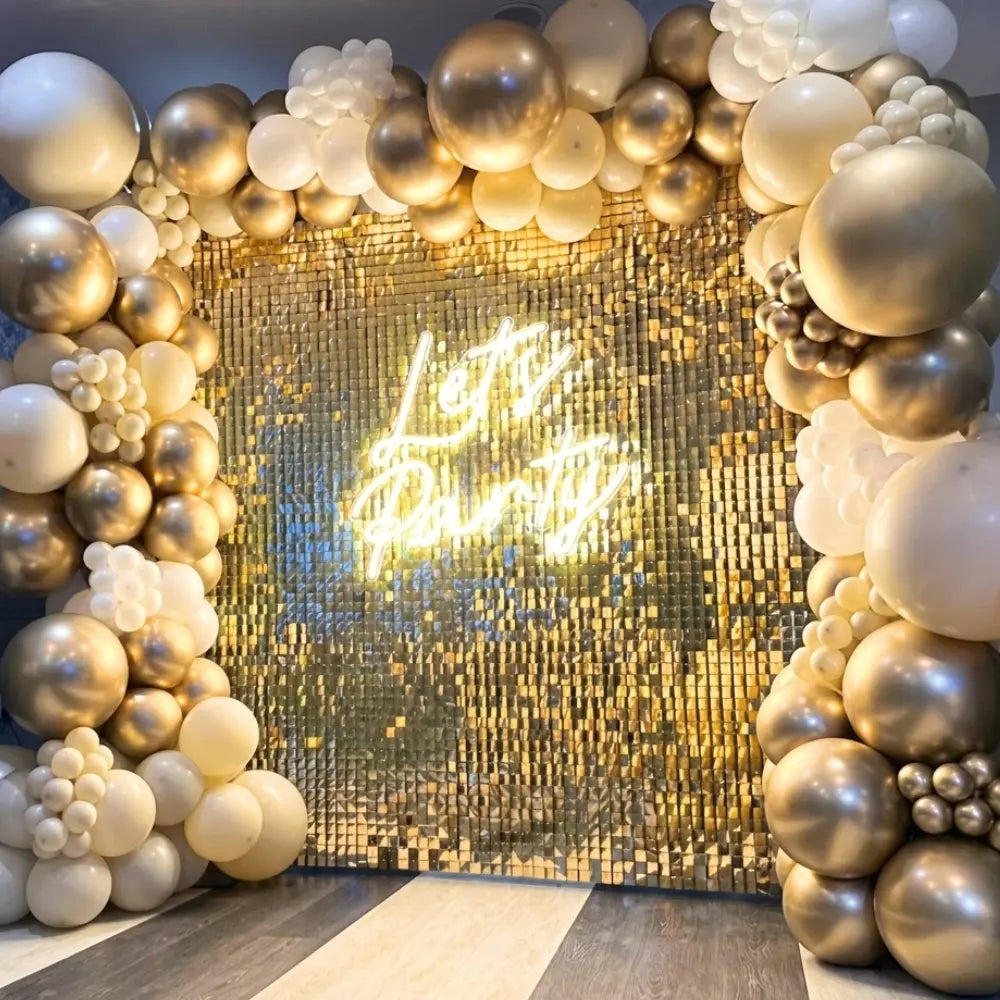 Sequin Wall backdrop with shiny gold tiles, ideal for events. Features a Let’s Party neon sign and balloon garland, excluding additional decorations.