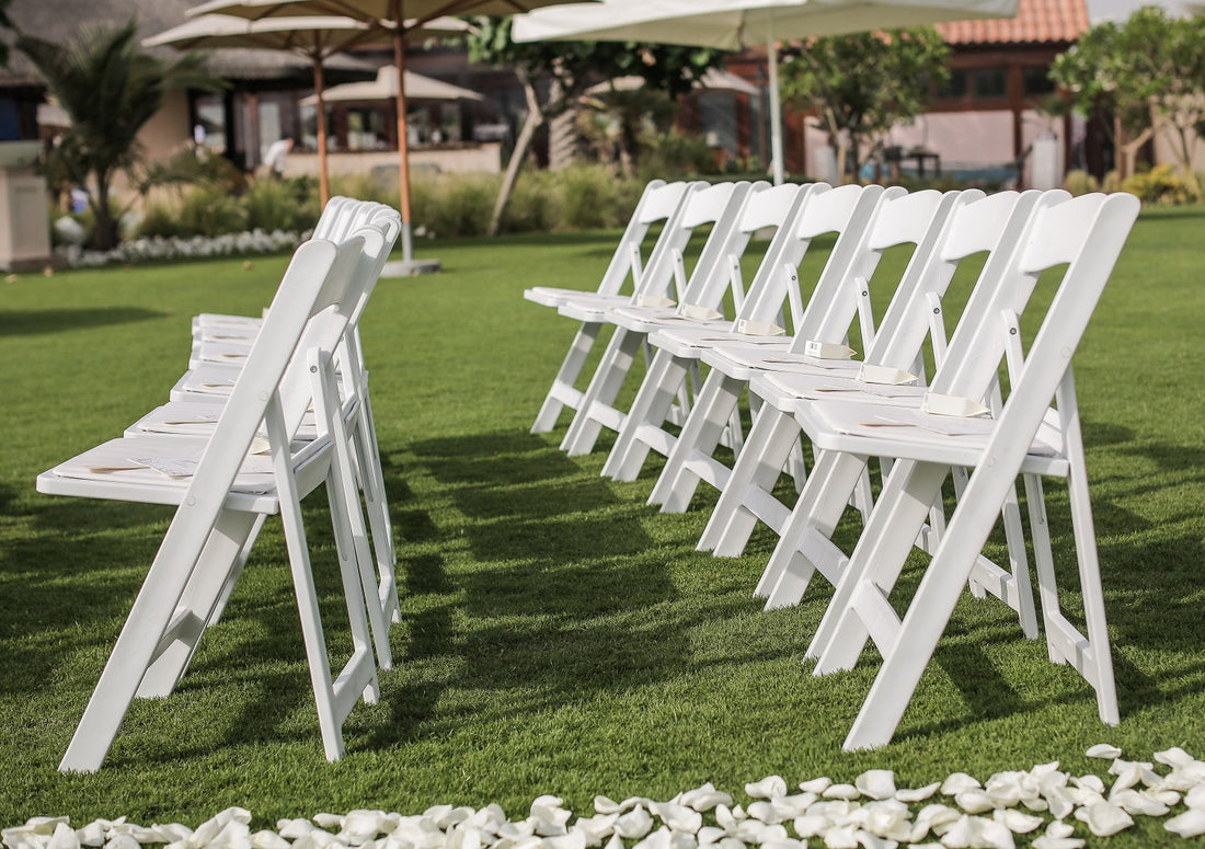 GARDEN CHAIR WHITE: A row of white resin foldable garden chairs on a lawn, ideal for versatile event seating at parties and weddings.