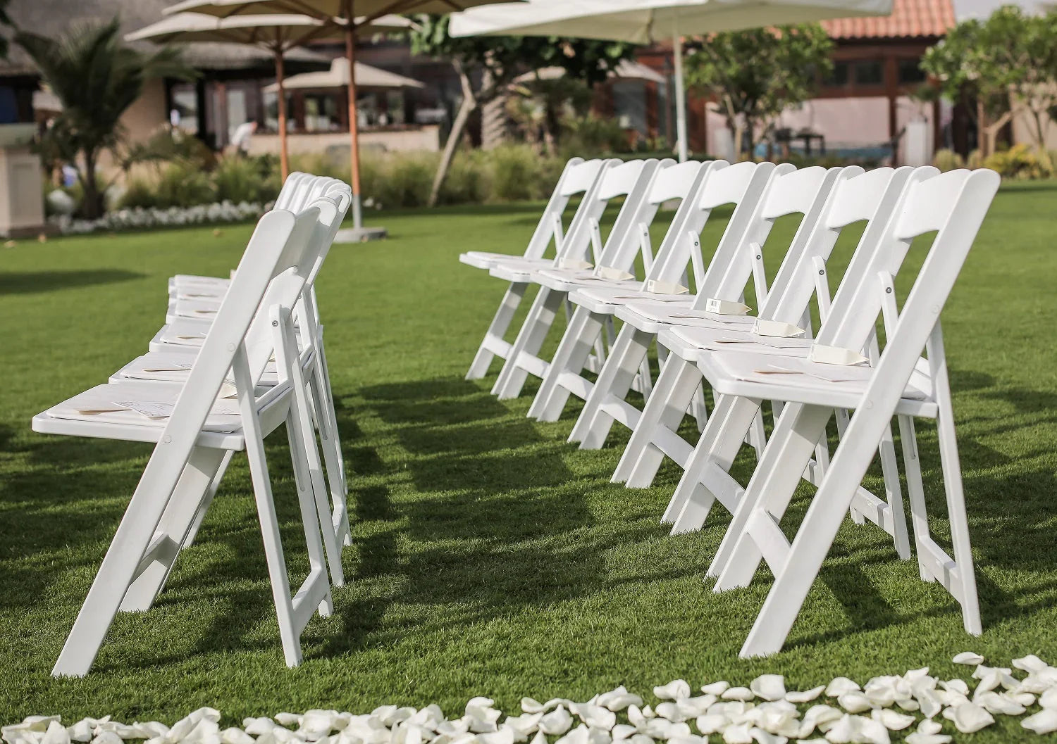 GARDEN CHAIR WHITE: A row of white resin foldable garden chairs on a lawn, ideal for versatile event seating at parties and weddings.