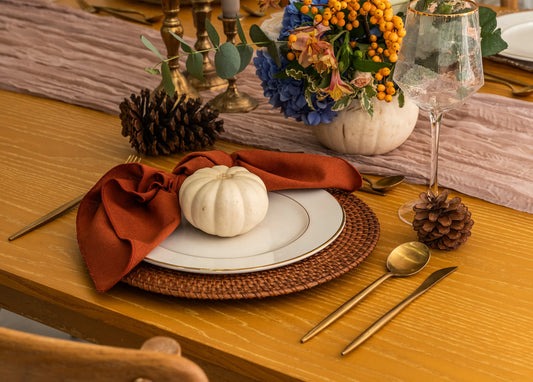 CHARGER PLATE - RATTAN on a fall-themed table setting with gold-rimmed dinnerware, a mini-pumpkin, brass flatware, and a rustic centerpiece.