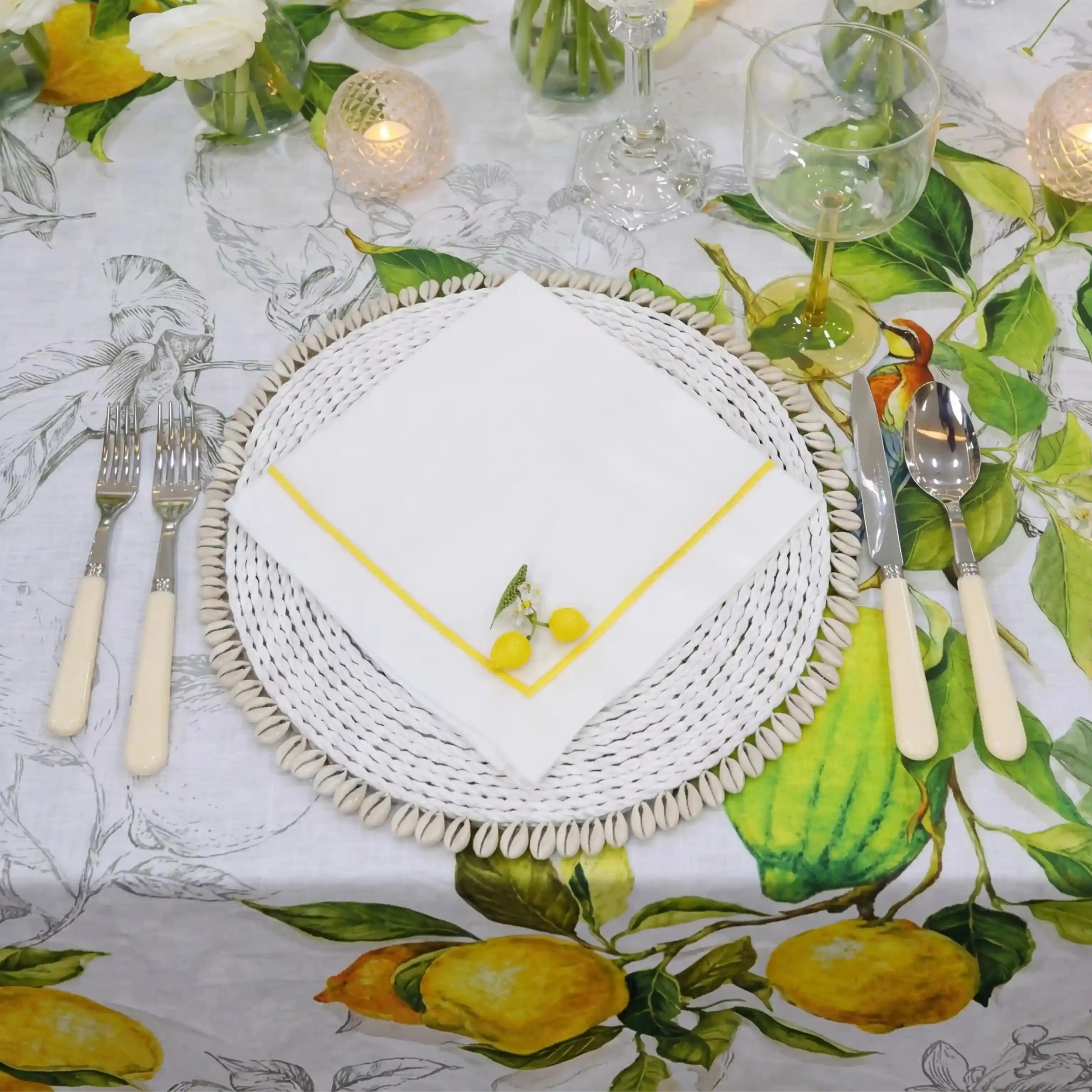 Table setting with white plates, cutlery, and a decorative napkin on a lemon-themed tablecloth.