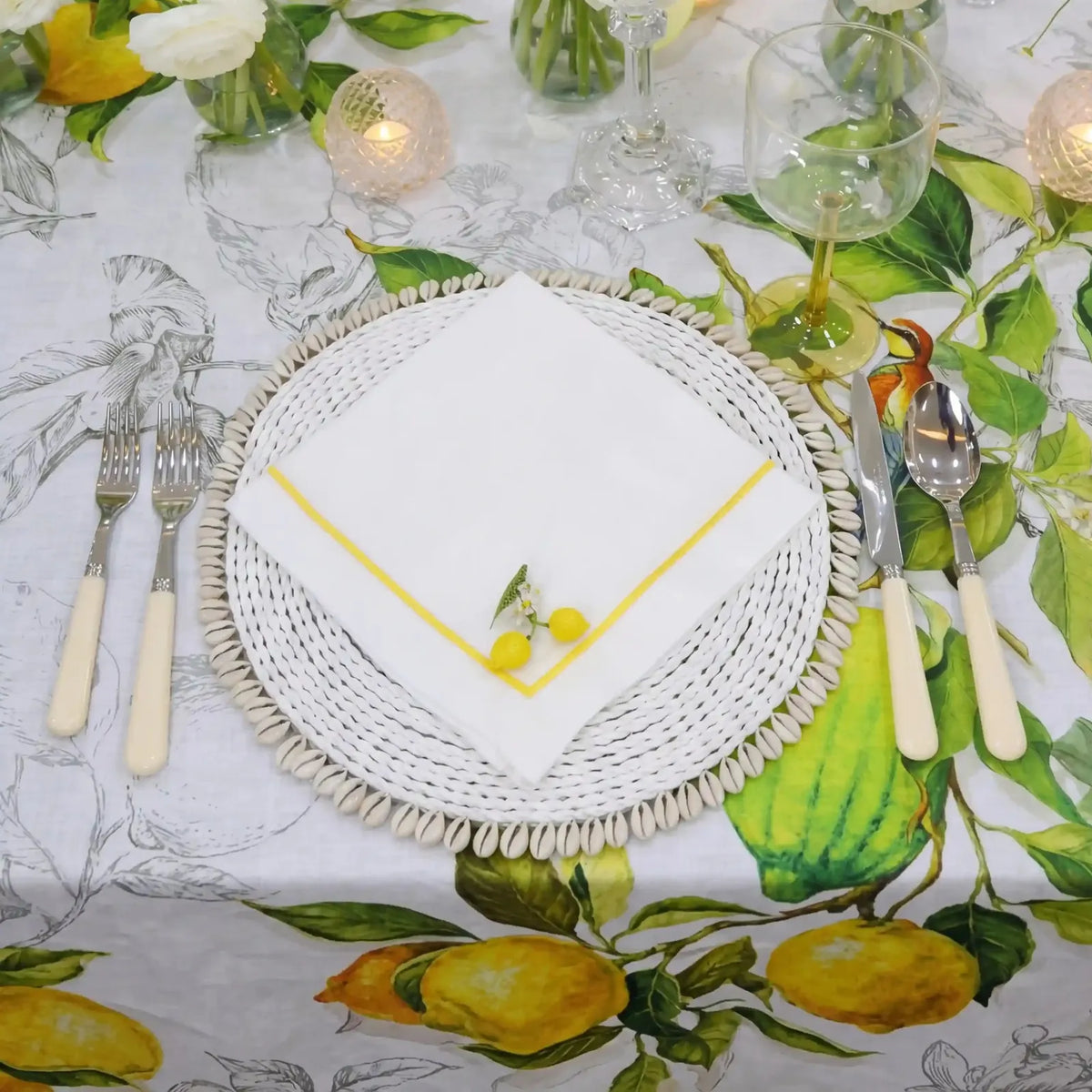 Table setting with white plates, cutlery, and a decorative napkin on a lemon-themed tablecloth.